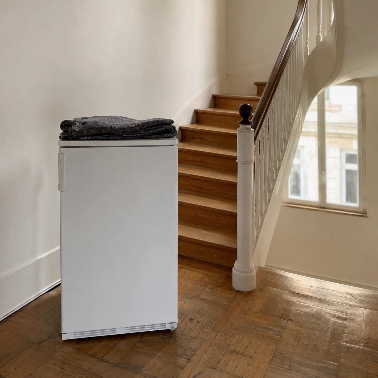 Un petit congélateur et sa couverture de protection à côté d’un escalier en bois.